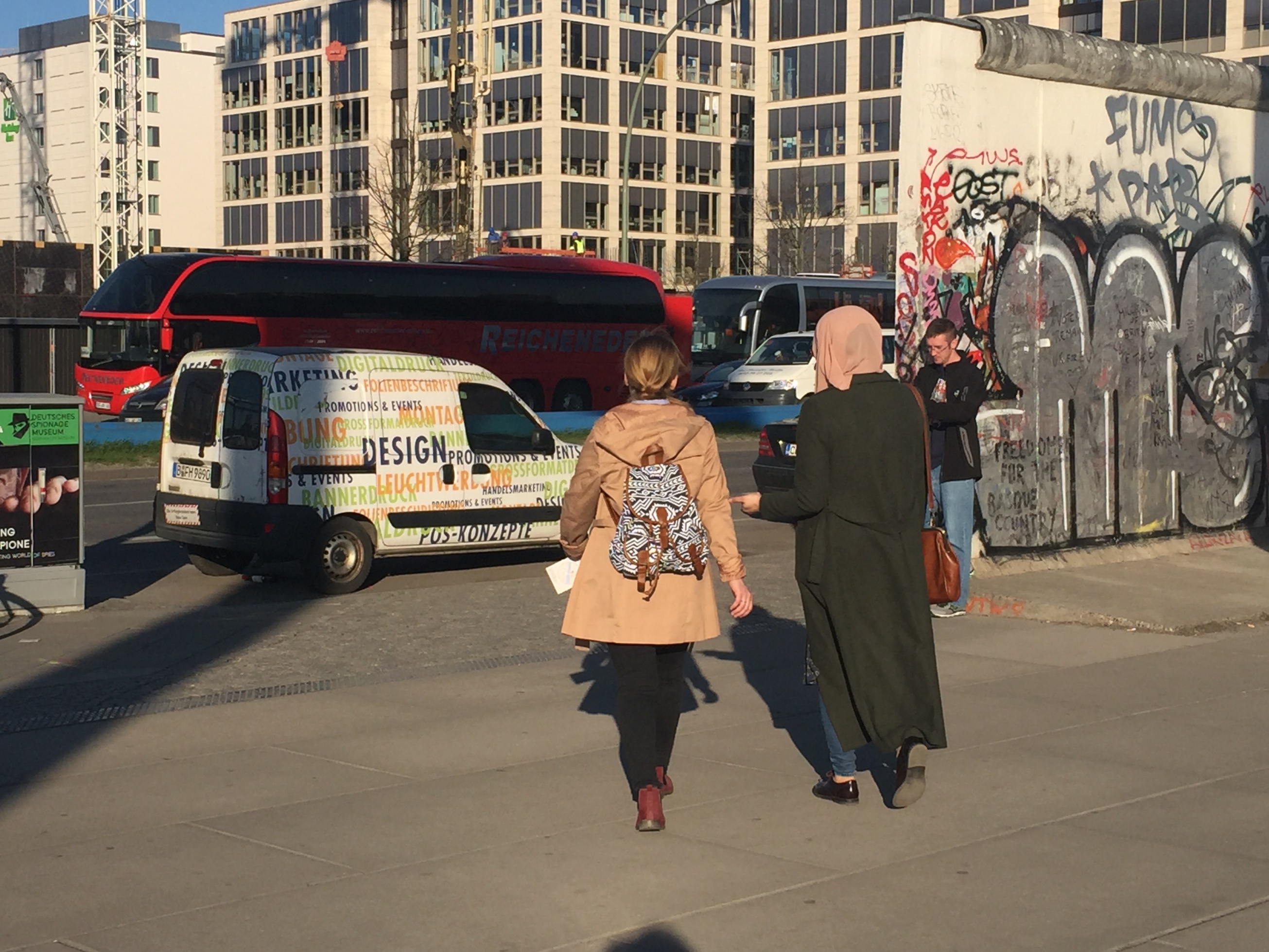 Due ragazze passeggiano a Berlino, vicino ai resti del muro che separava l’Est dall’Ovest